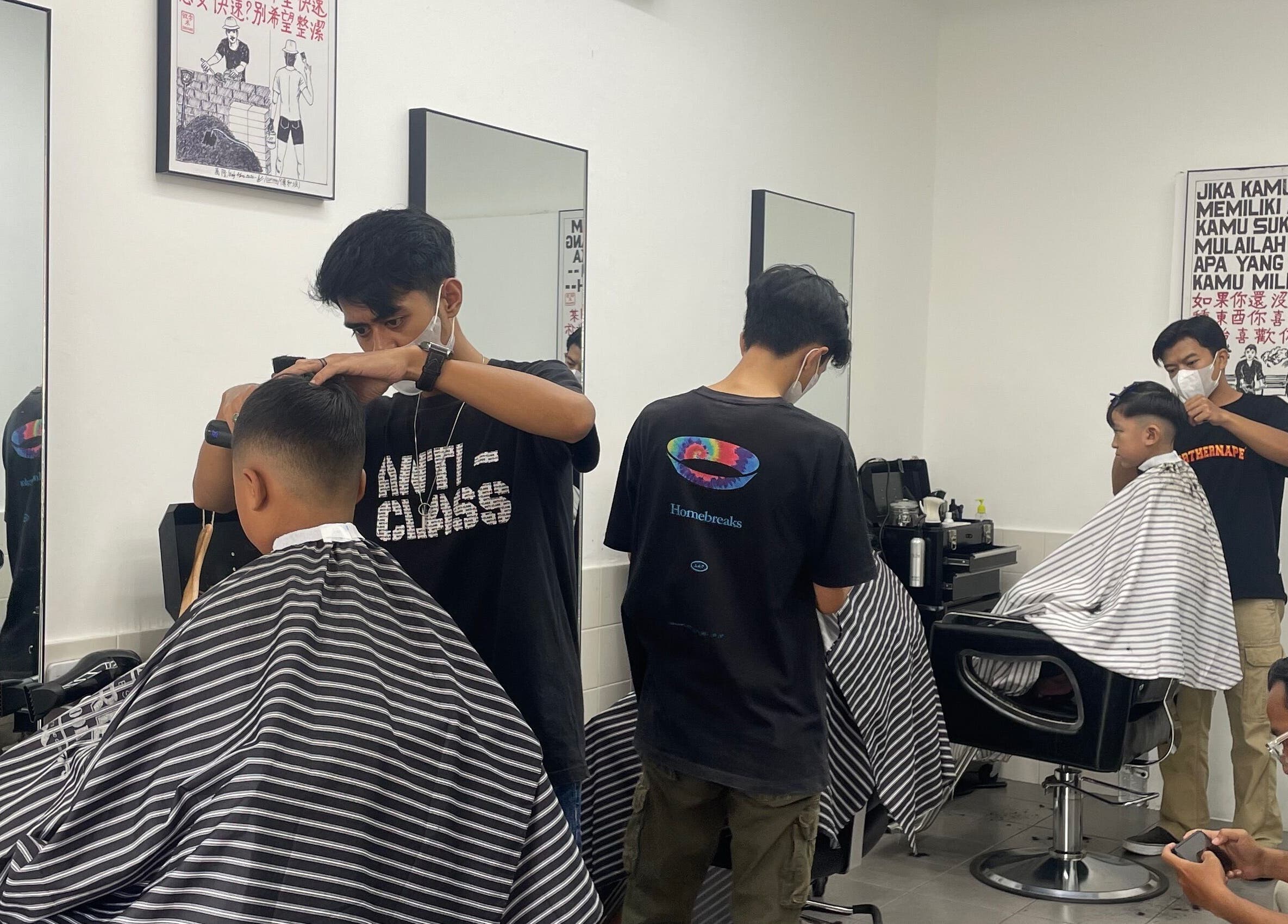 Penata rambut di MYC Haircuts, Jawa Barat, ID, memberikan potongan rambut modern pada pelanggan muda.