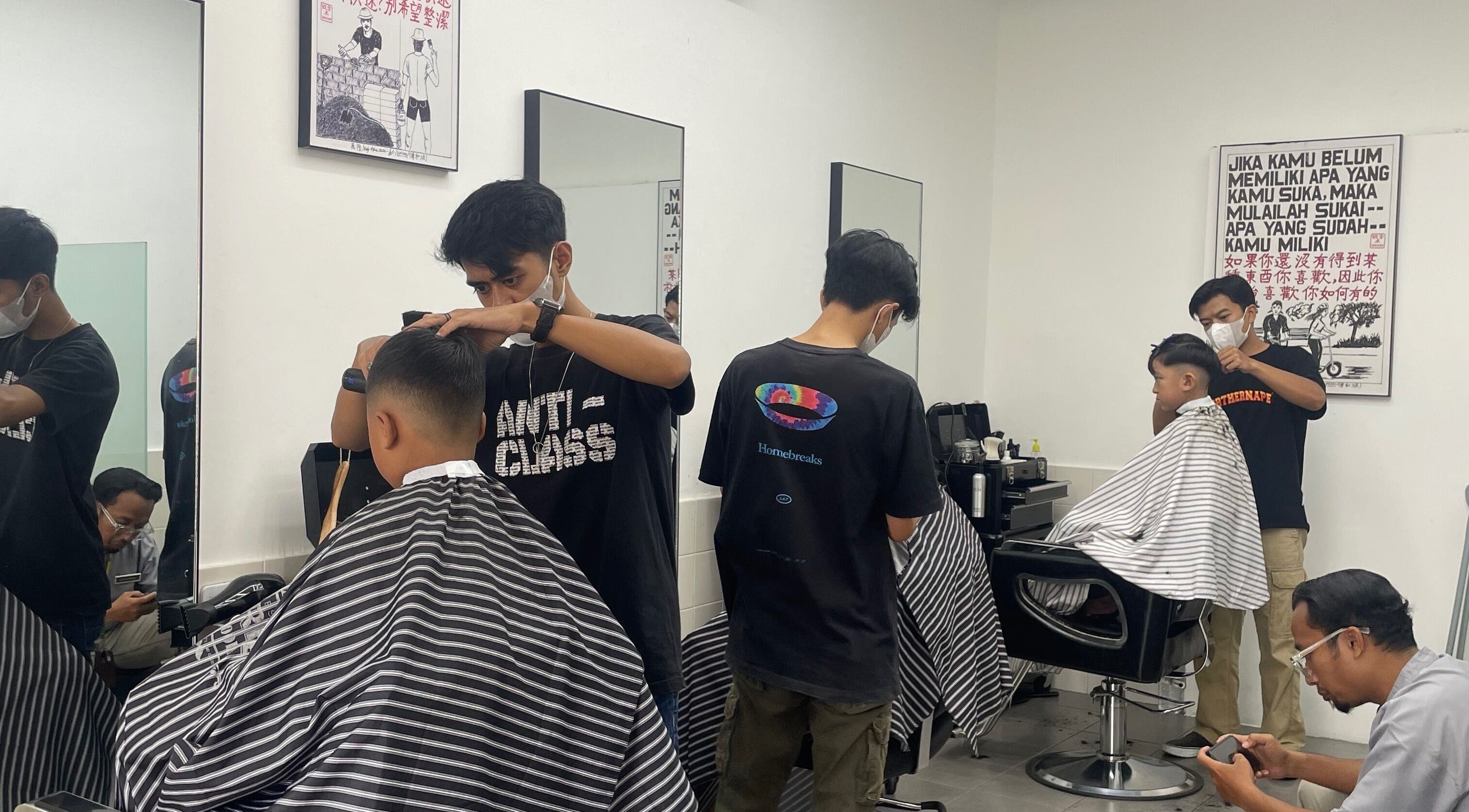 Penata rambut di MYC Haircuts, Jawa Barat, ID, memberikan potongan rambut modern pada pelanggan muda.