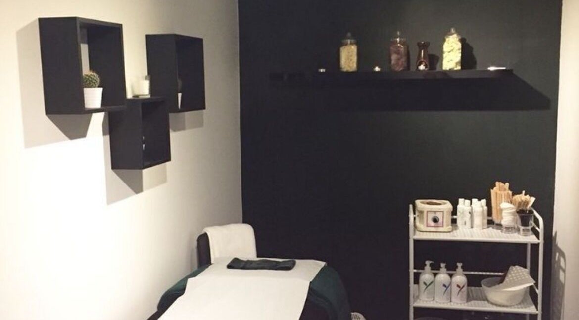 Treatment room at The Lash Alchemist in Montego Bay, St. James Parish, JM with a bed and shelves.