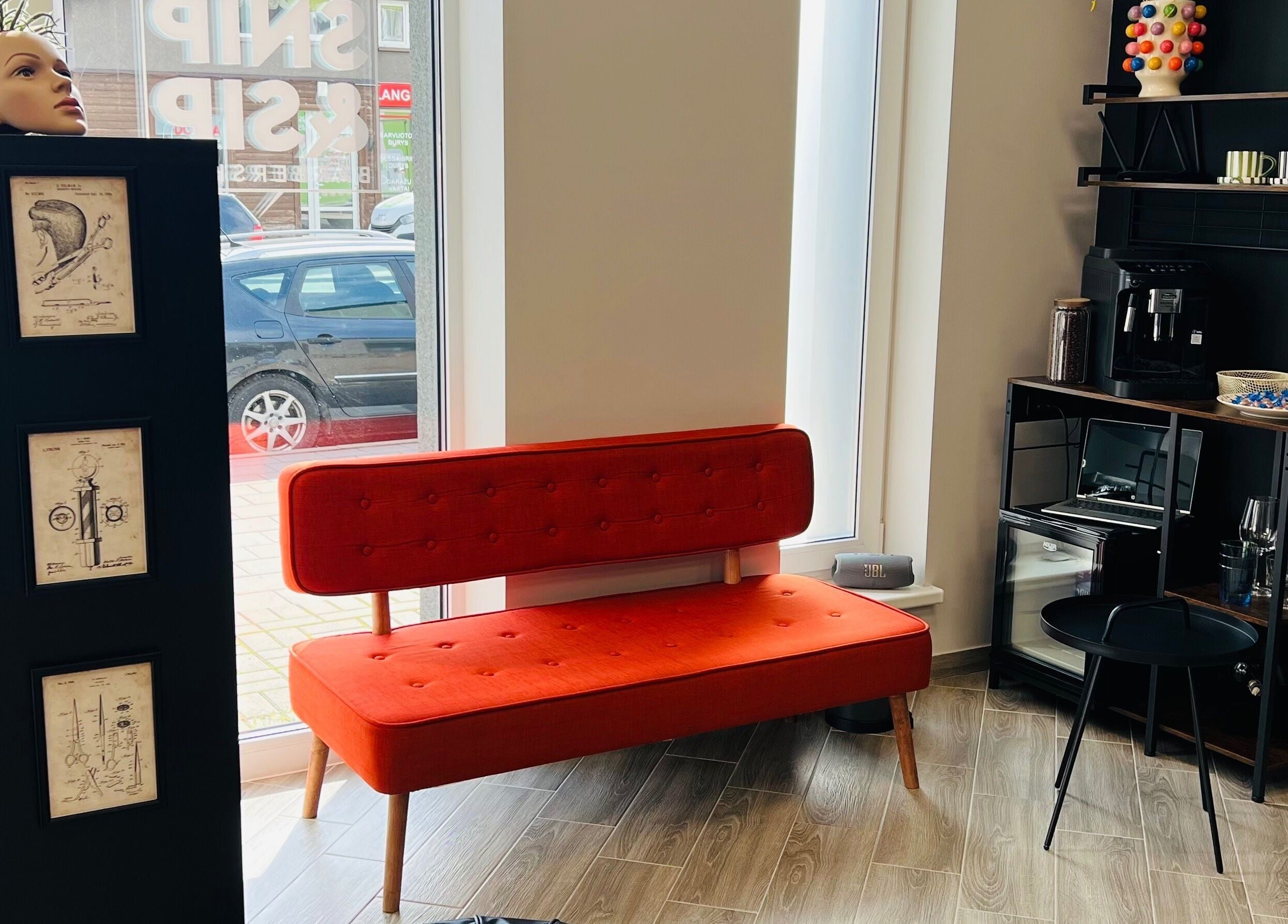 Jaukiai įrengtas kampas Snip&Sip Barbershop Panevėžyje su raudona sofa ir kava.