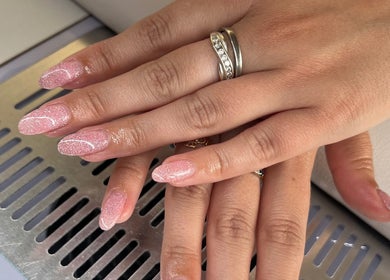 Elegant pink glitter nails at AJ Beauty, Bath, England, GB. Perfectly manicured hands showcasing intricate nail art.