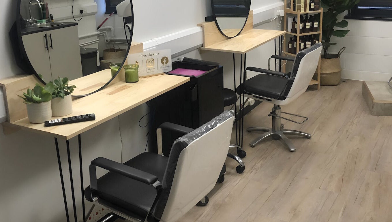 Modern salon chairs at PhedeliaRose, London, England, GB, with mirrors and plants on wooden desks.