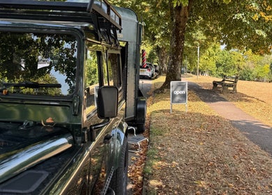 Shelly The Barber's mobile service in Newport, Wales, GB. A tranquil roadside setup with lush trees.
