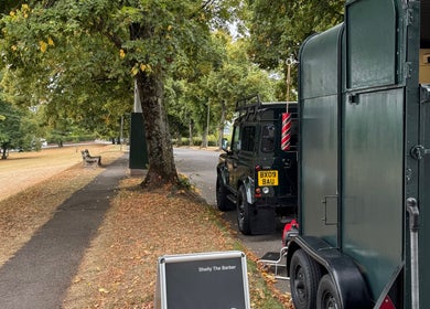 Shelly The Barber mobile trailer in Newport, Wales, GB, near a park with lush green trees.