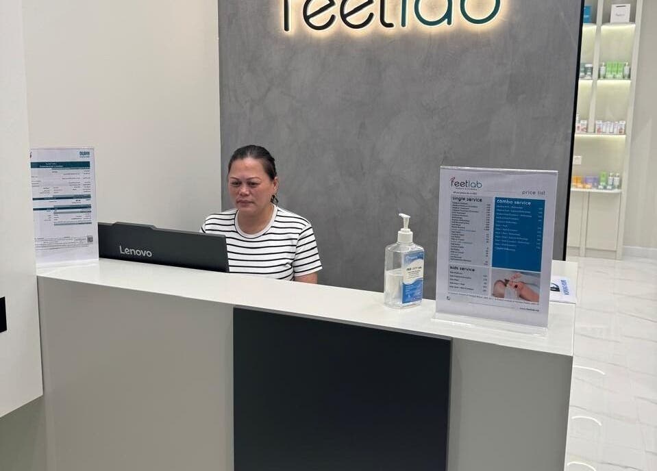 Reception desk of Feetlab - Dubai Creek Harbour, Dubai, AE with staff and service menu displayed.