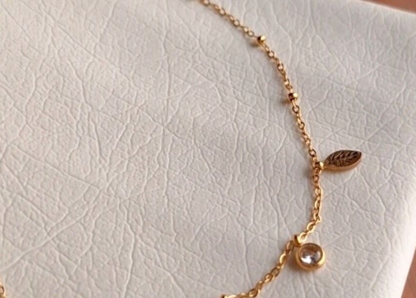 Elegant gold bracelet with delicate charms on a textured surface at nail art, Tehran, IR.