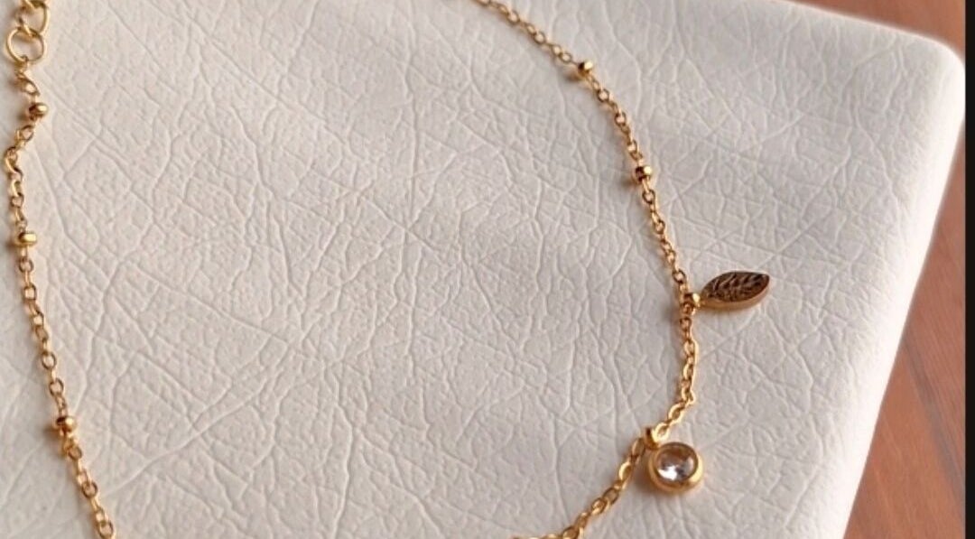 Elegant gold bracelet with delicate charms on a textured surface at nail art, Tehran, IR.