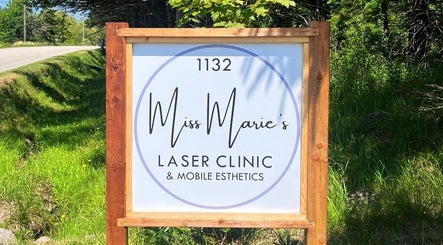 Sign of Miss Marie’s Laser Clinic near roadside at Brooklyn, Nova Scotia, CA, surrounded by greenery.