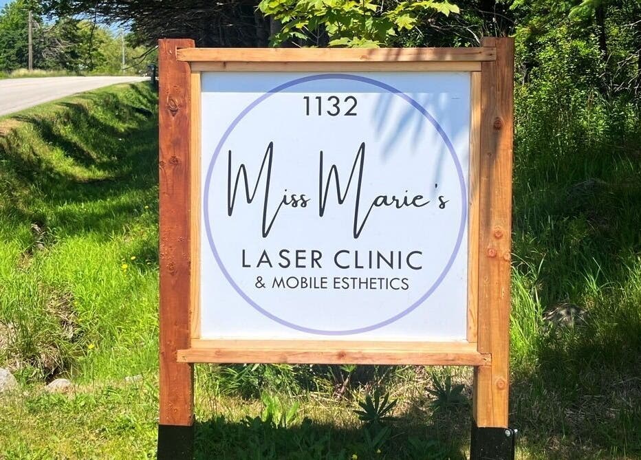 Street view of Miss Marie’s Laser Clinic sign at 1132 Brooklyn, Nova Scotia, CA amidst lush greenery.