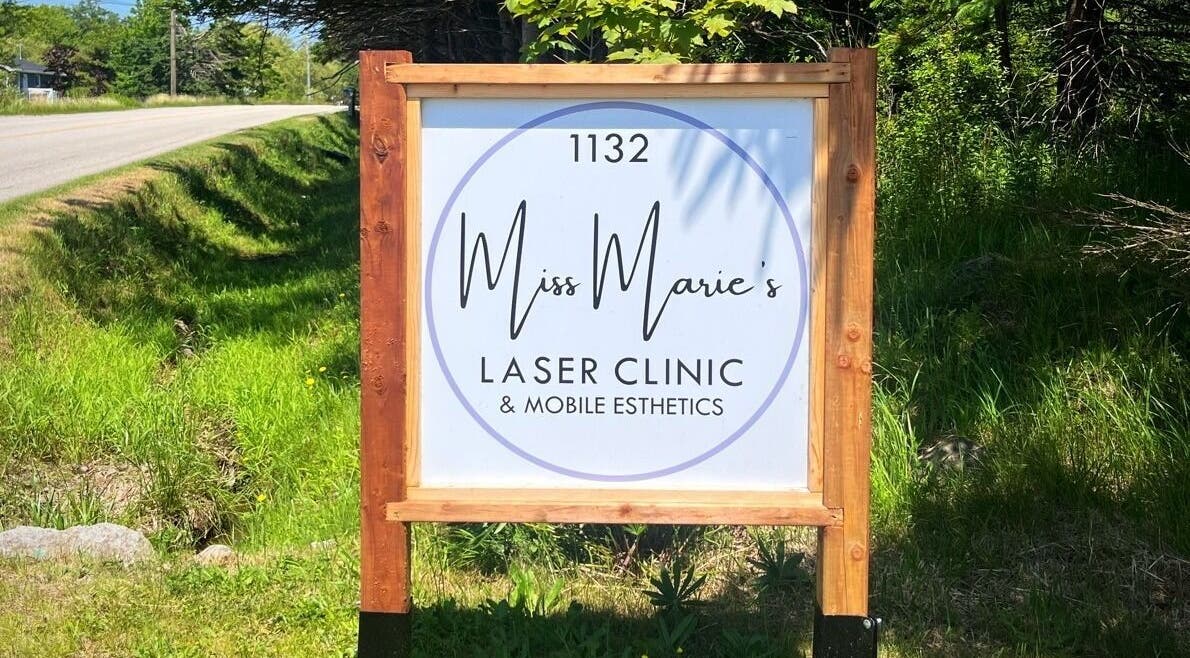 Street view of Miss Marie’s Laser Clinic sign at 1132 Brooklyn, Nova Scotia, CA amidst lush greenery.