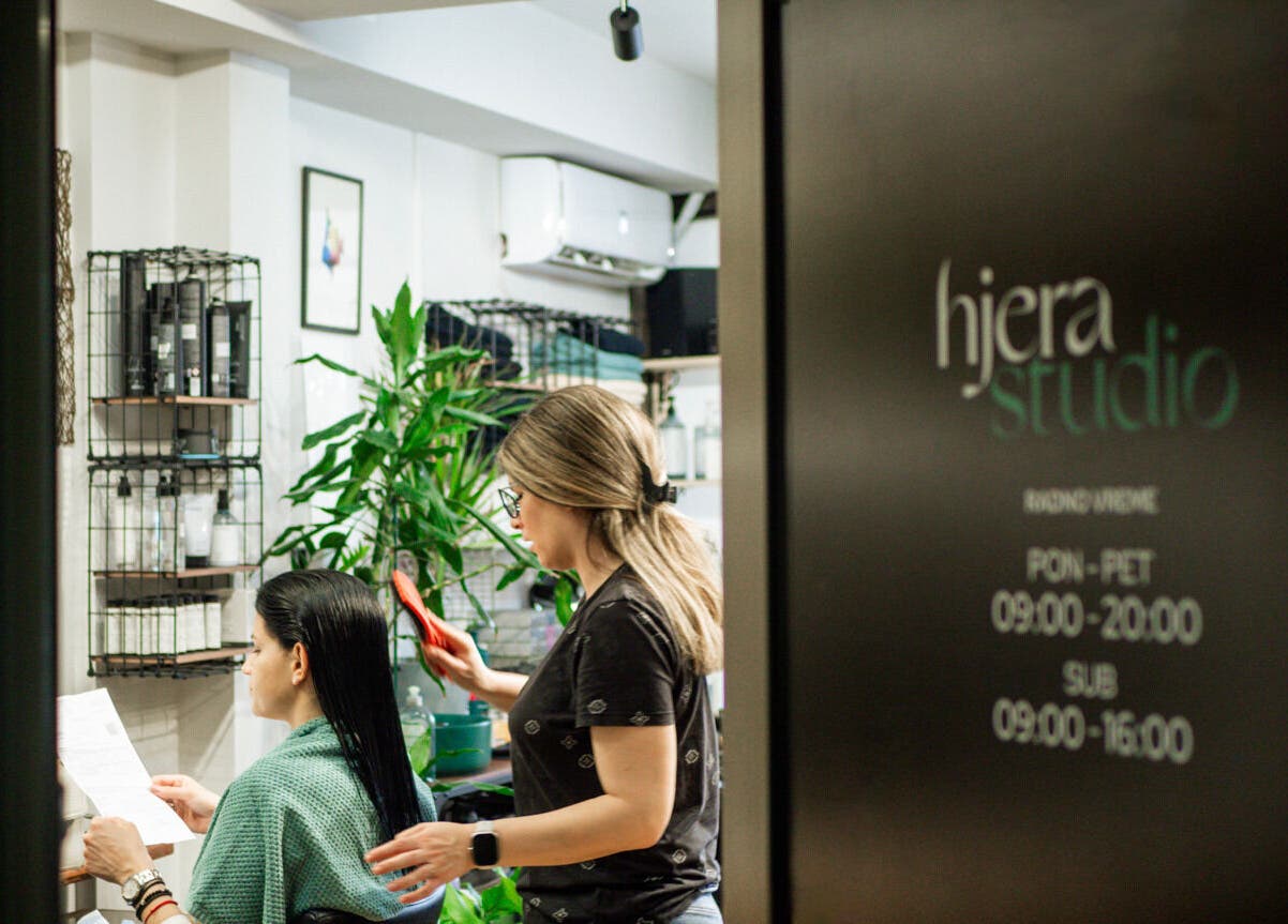 Stylist works on client's hair at Hjera Studio & Spa in Beograd, RS, showcasing elegant and modern decor.