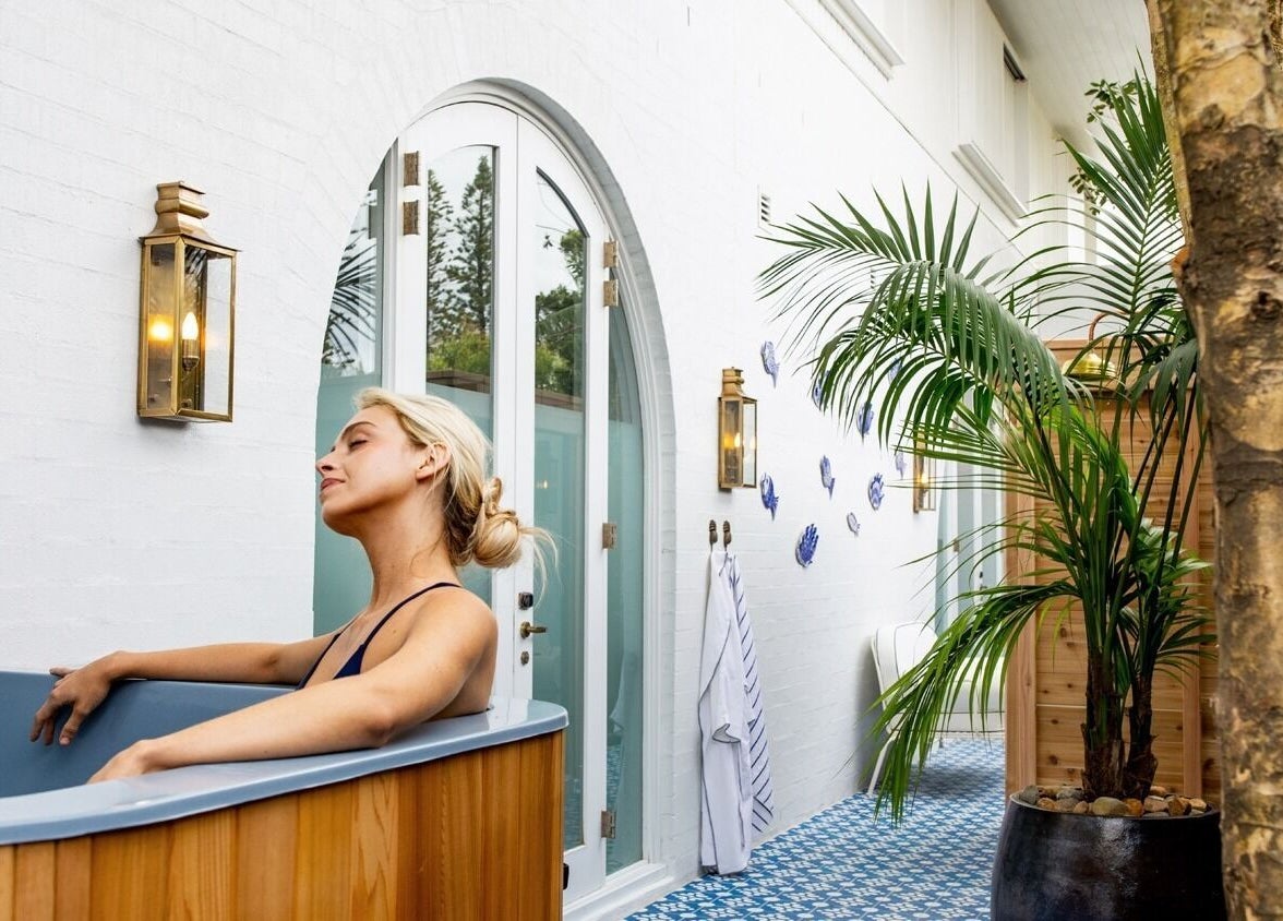 Woman relaxes in outdoor bath at Halcyon Wellness, Cabarita Beach, New South Wales, AU, surrounded by lush greenery.