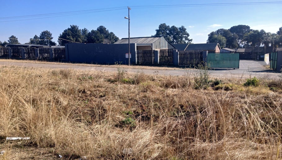 Boundary fence of BusiNails in Centurion, Gauteng, ZA, lined with trees under a clear blue sky.