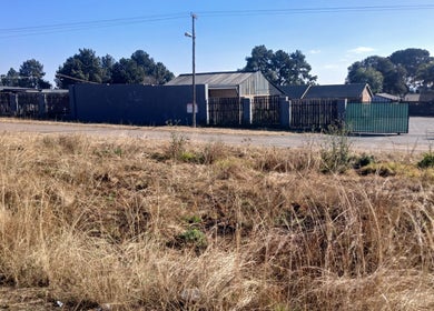 Boundary fence of BusiNails in Centurion, Gauteng, ZA, lined with trees under a clear blue sky.