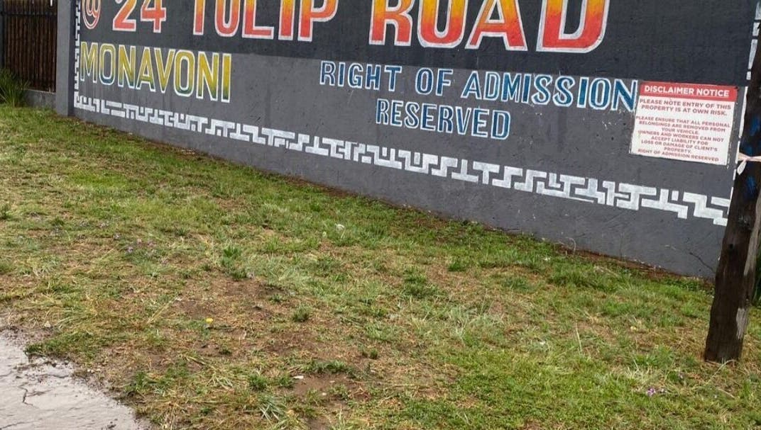 Street sign for BusiNails at 24 Tulip Road, Centurion, Gauteng, ZA, against a grassy foreground.