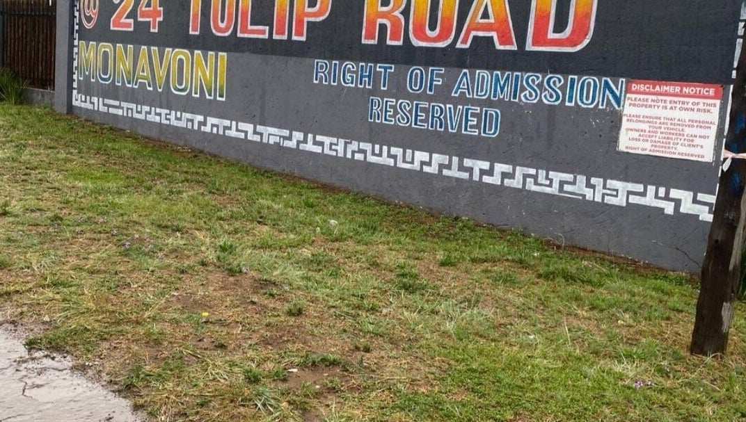 Street sign for BusiNails at 24 Tulip Road, Centurion, Gauteng, ZA, against a grassy foreground.