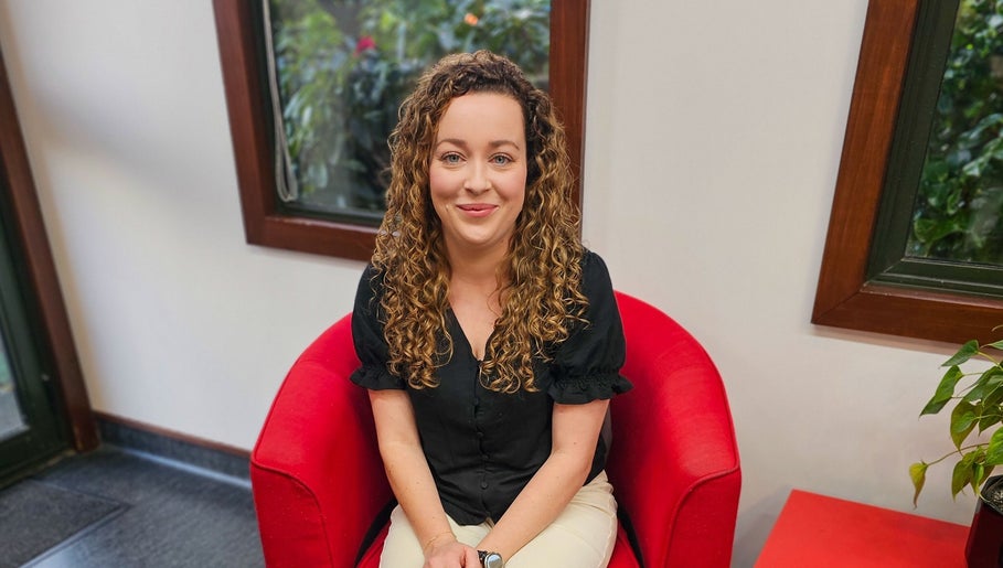 Person seated in a red chair at HairbyMrsBlades, Porirua, Wellington Region, NZ.