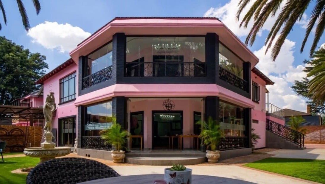 Exterior of CheZel & Co in Springs, Gauteng, ZA with pink facade, lush lawn, and sculpture.