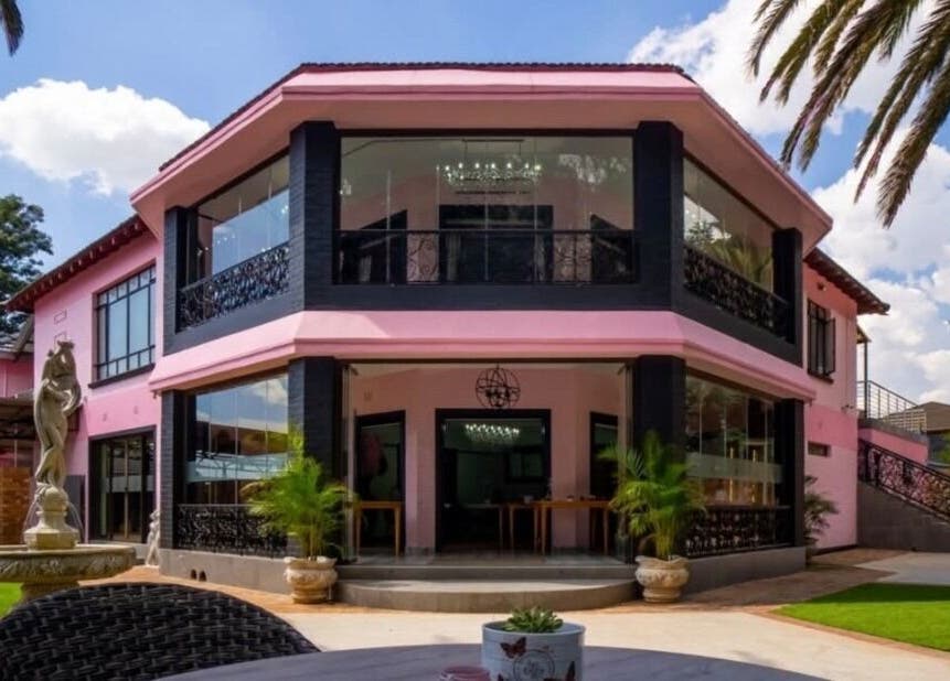 Exterior of CheZel & Co in Springs, Gauteng, ZA with pink facade, lush lawn, and sculpture.