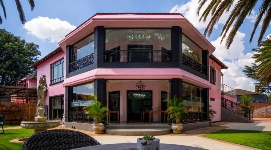 Exterior of CheZel & Co in Springs, Gauteng, ZA with pink facade, lush lawn, and sculpture.