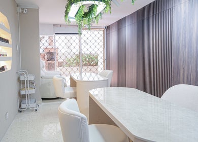 Interior elegante de salón en Fiore Studio, Barranquilla, Atlántico, CO con sillas blancas y estantes de esmaltes.