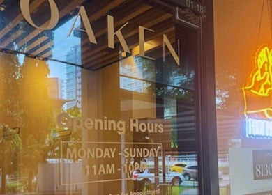 Front view of Oaken in Singapore, SG showing glass door with signage and neon massage icon.