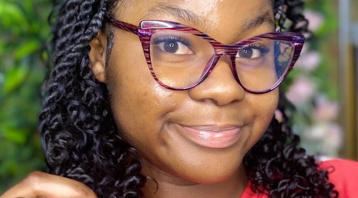 Smiling woman with stylish glasses at The Hair Topic in Portmore, St. Catherine Parish, JM.