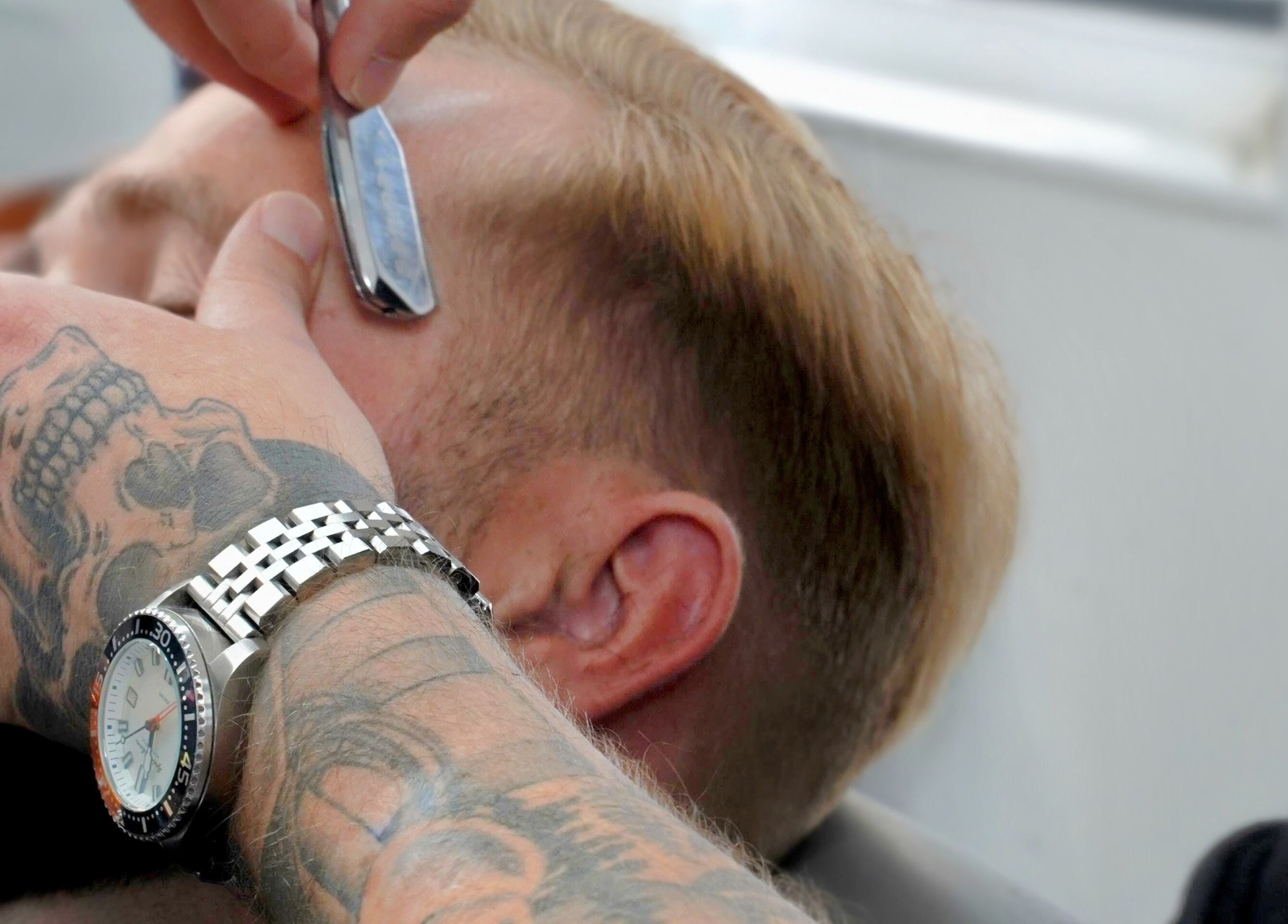 Close-up of shaving at Barber Boy Studio, Horsham, England, GB. Tattooed hand skillfully holds straight razor.
