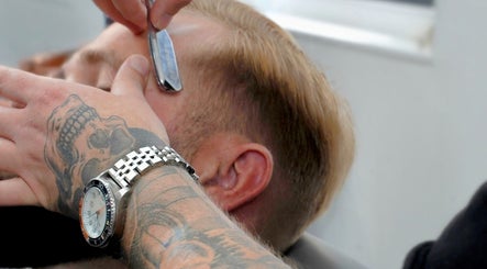 Close-up of shaving at Barber Boy Studio, Horsham, England, GB. Tattooed hand skillfully holds straight razor.