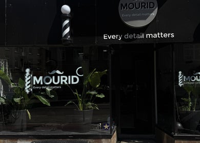 Front view of Mourid West in Amsterdam, Noord-Holland, NL, showcasing sleek black signage and green plants.