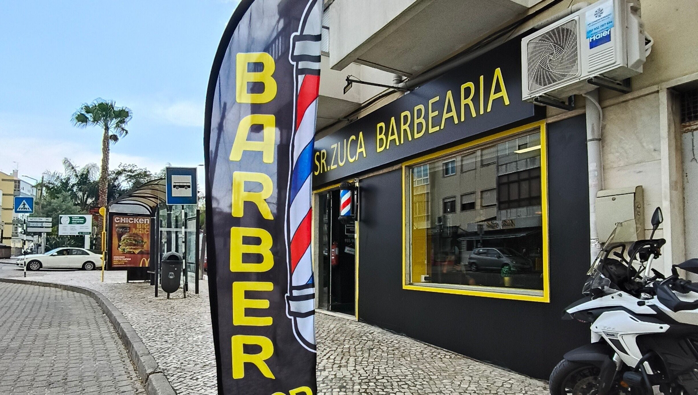 Entrada da Sr. Zuca Barbearia em Amora, Setúbal, PT com letreiro e bandeira de barbearia.
