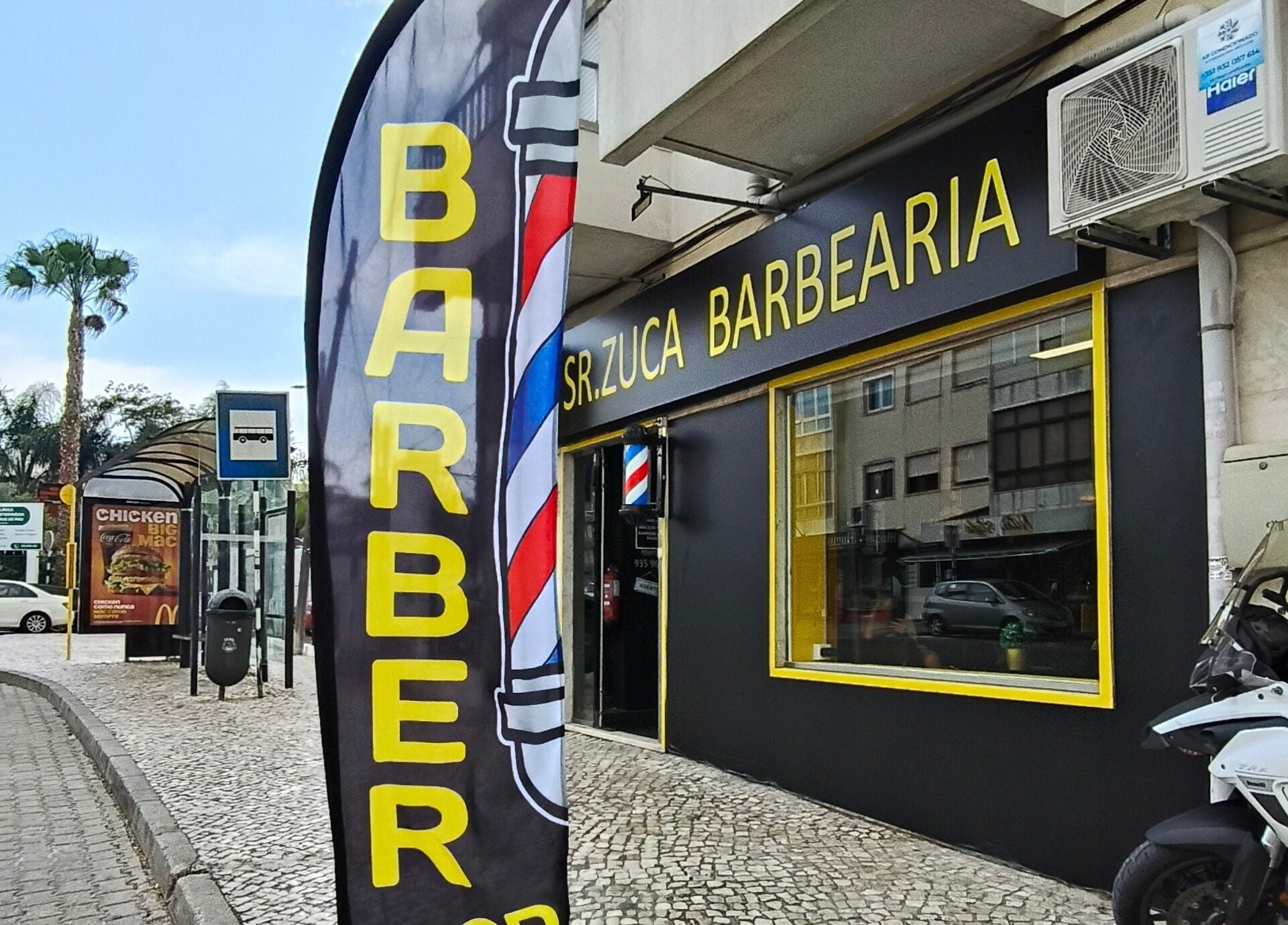 Entrada da Sr. Zuca Barbearia em Amora, Setúbal, PT com letreiro e bandeira de barbearia.