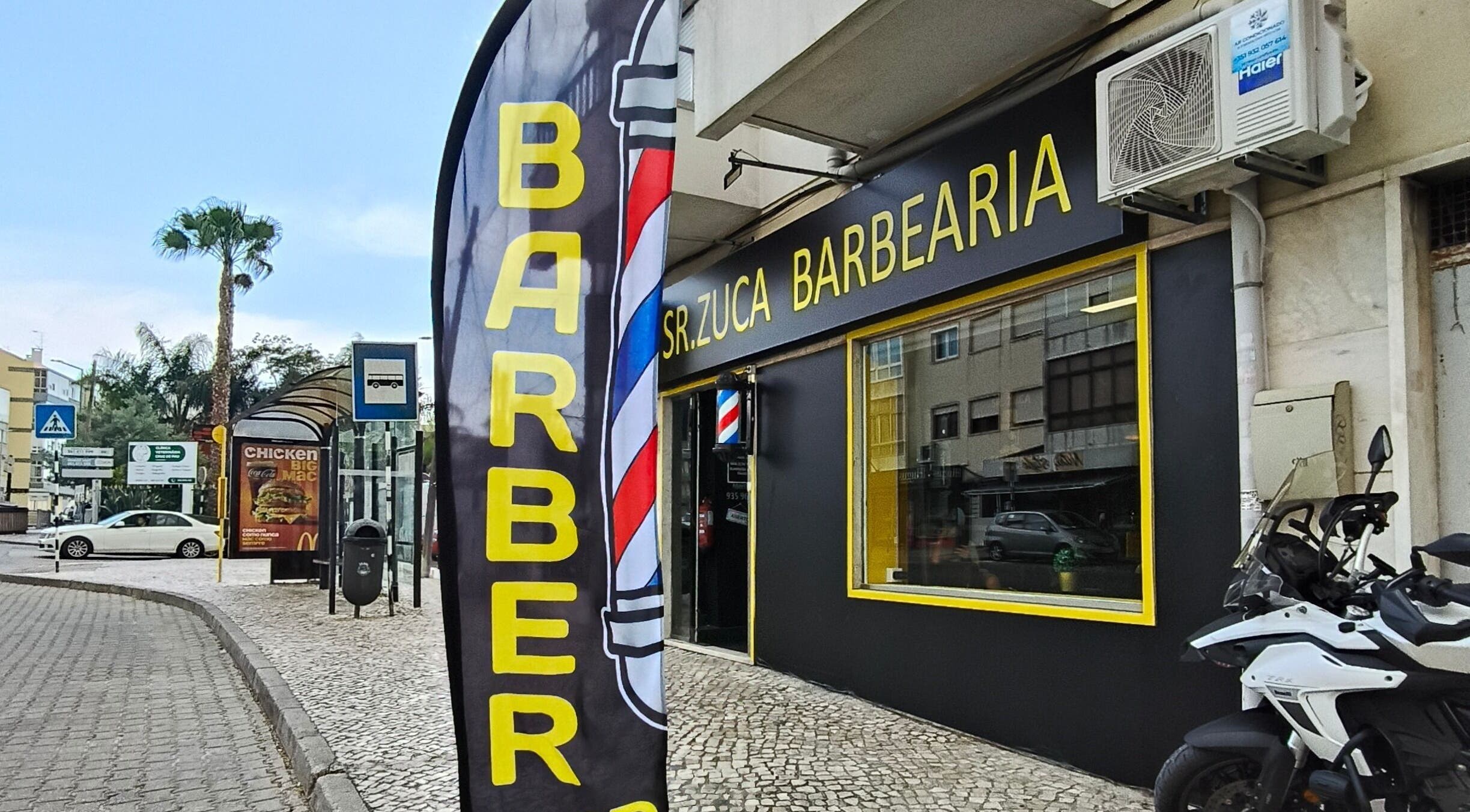 Entrada da Sr. Zuca Barbearia em Amora, Setúbal, PT com letreiro e bandeira de barbearia.