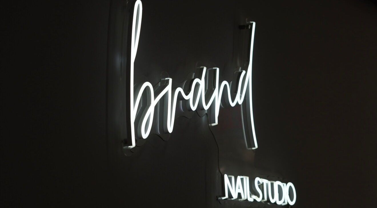 Illuminated neon sign of Brand Nail Studio in Philadelphia, Pennsylvania, US on a dark background.