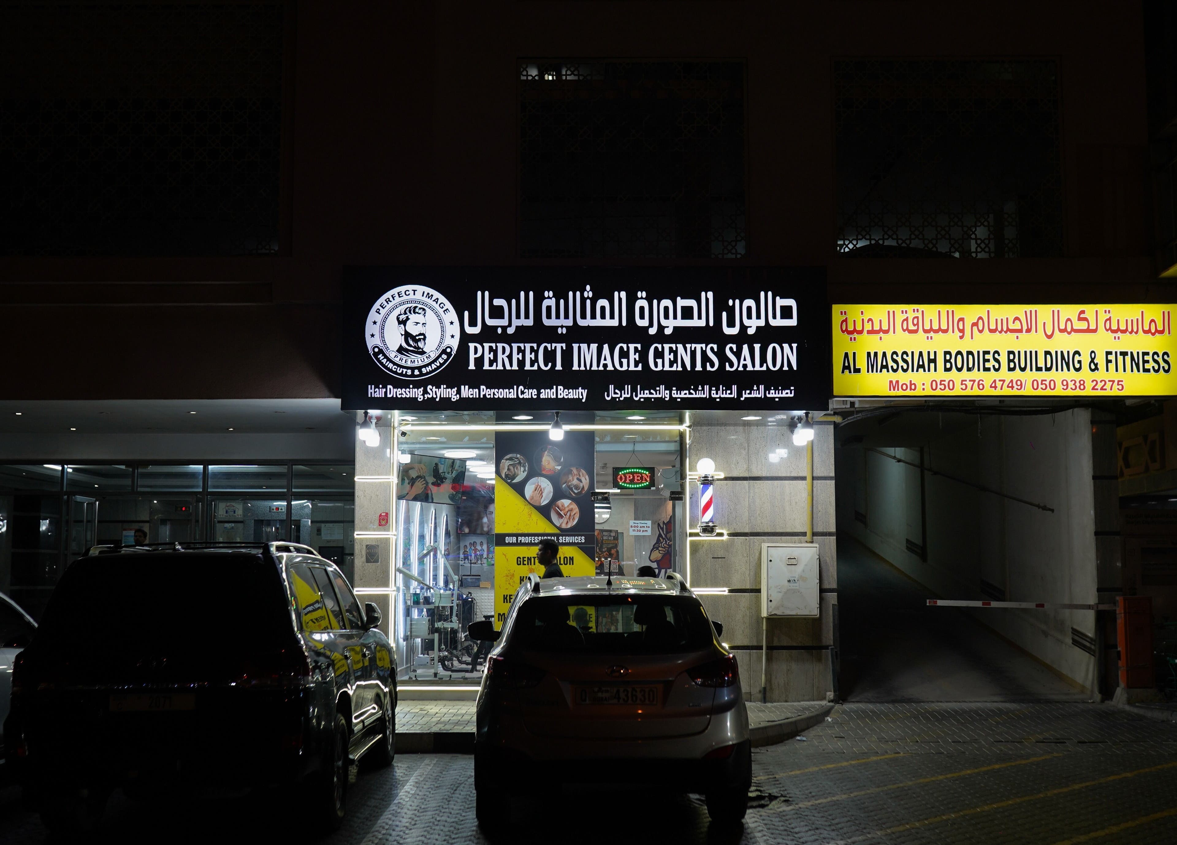 Exterior of Perfect Image Gents Salon in Sharjah, Sharjah, AE, well-lit at night with signage and parked cars.