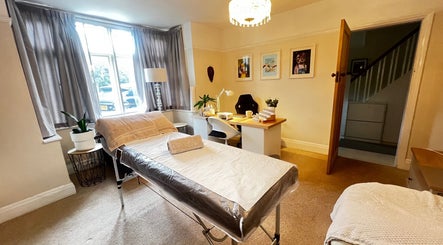 Cozy treatment room at Lumiere Beauty, Cambridge, England with massage bed, desk, and warm lighting.