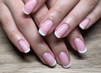Close-up of a classic French manicure at Lumiere Beauty, Cambridge, England, GB on a wooden surface.