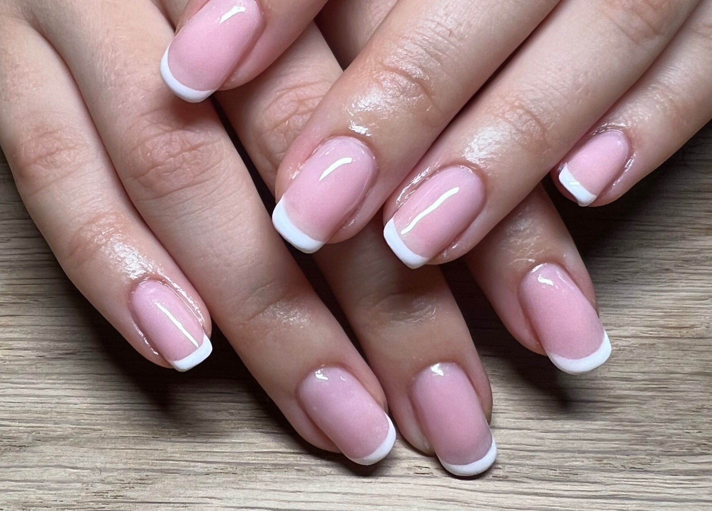 Close-up of a classic French manicure at Lumiere Beauty, Cambridge, England, GB on a wooden surface.