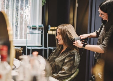 Stylist perfecting hair at Alchemy & I Berkhamsted, England, GB with a radiant client smiling.