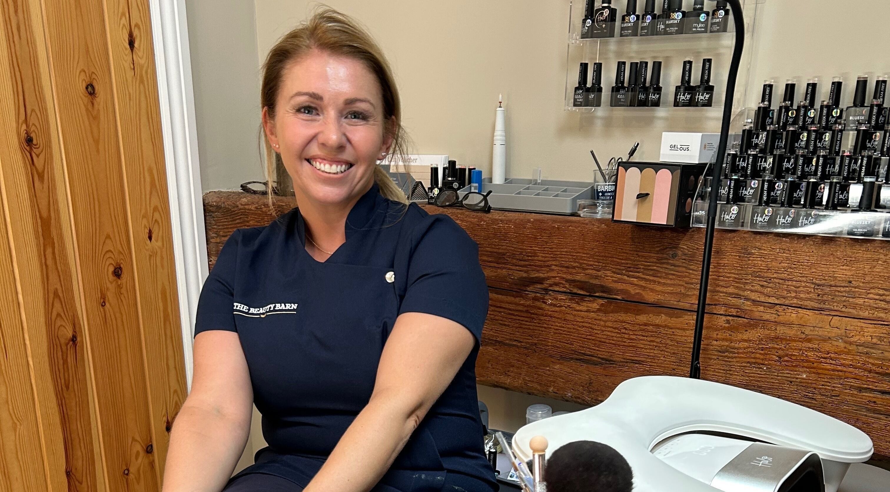 Smiling stylist at The Beauty Barn, Wilton, England, GB, surrounded by nail products.