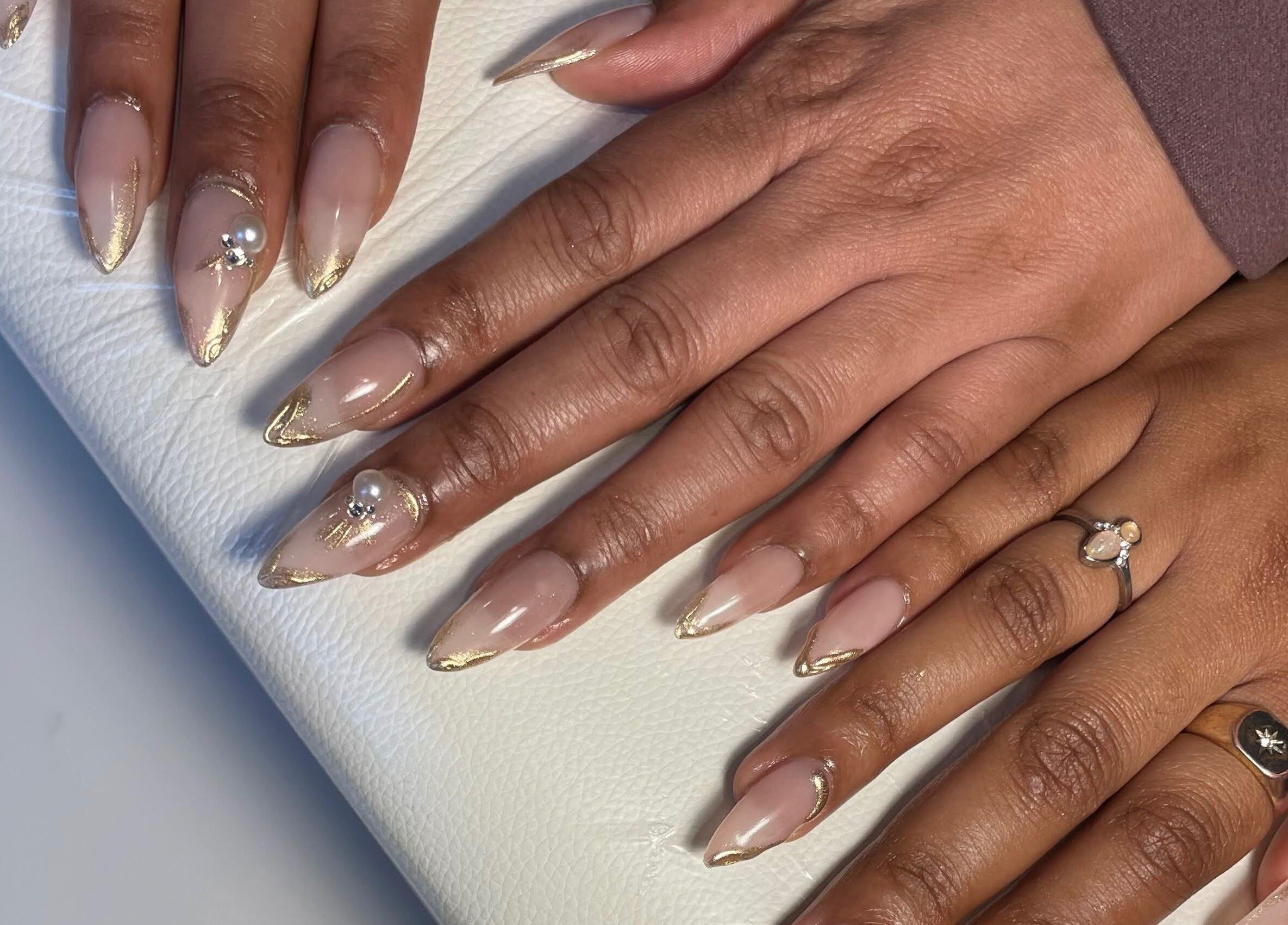 Nail art raffiné à Le Saphyr, Montréal, Québec, CA, avec des touches dorées et perles élégantes.