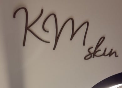 KM Skin logo on wall at Clydebank, Scotland, GB. Elegant scripted font highlights beauty focus.