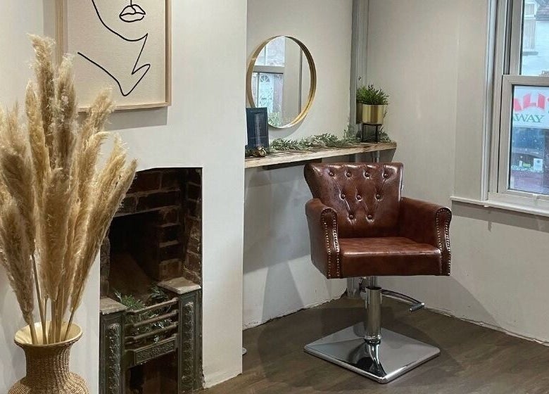 A stylish chair in Salon Pickle, Bromsgrove, England, GB, next to a decorative vase and mirror.