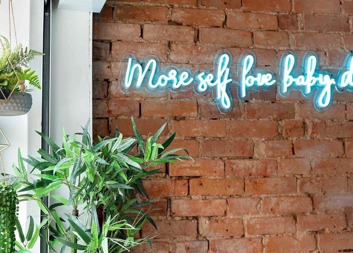 Neon sign 'More self love' at Salon Pickle, Bromsgrove, England, GB, with vibrant plants and brick wall backdrop.