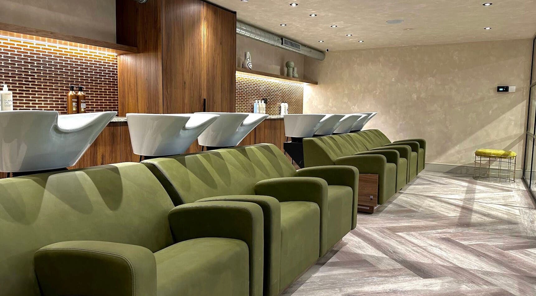 Modern salon seating area at Rowan Ireland Hair, London, England, GB with green chairs and washing stations.