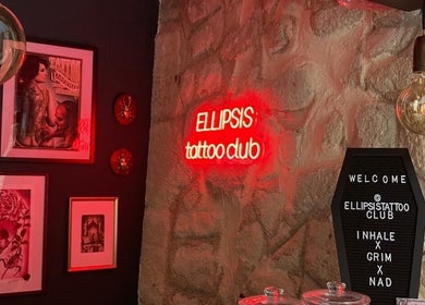 Cozy interior of Ellipsis Tattoo Club in Paris, Île-de-France, FR with neon sign and framed art.