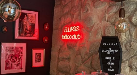 Cozy interior of Ellipsis Tattoo Club in Paris, Île-de-France, FR with neon sign and framed art.