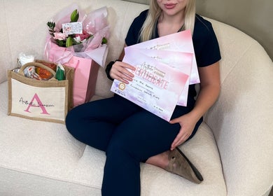 Woman holding certificates from Aesthetic Invasion, Liverpool, England, GB, seated with flowers and a branded bag.