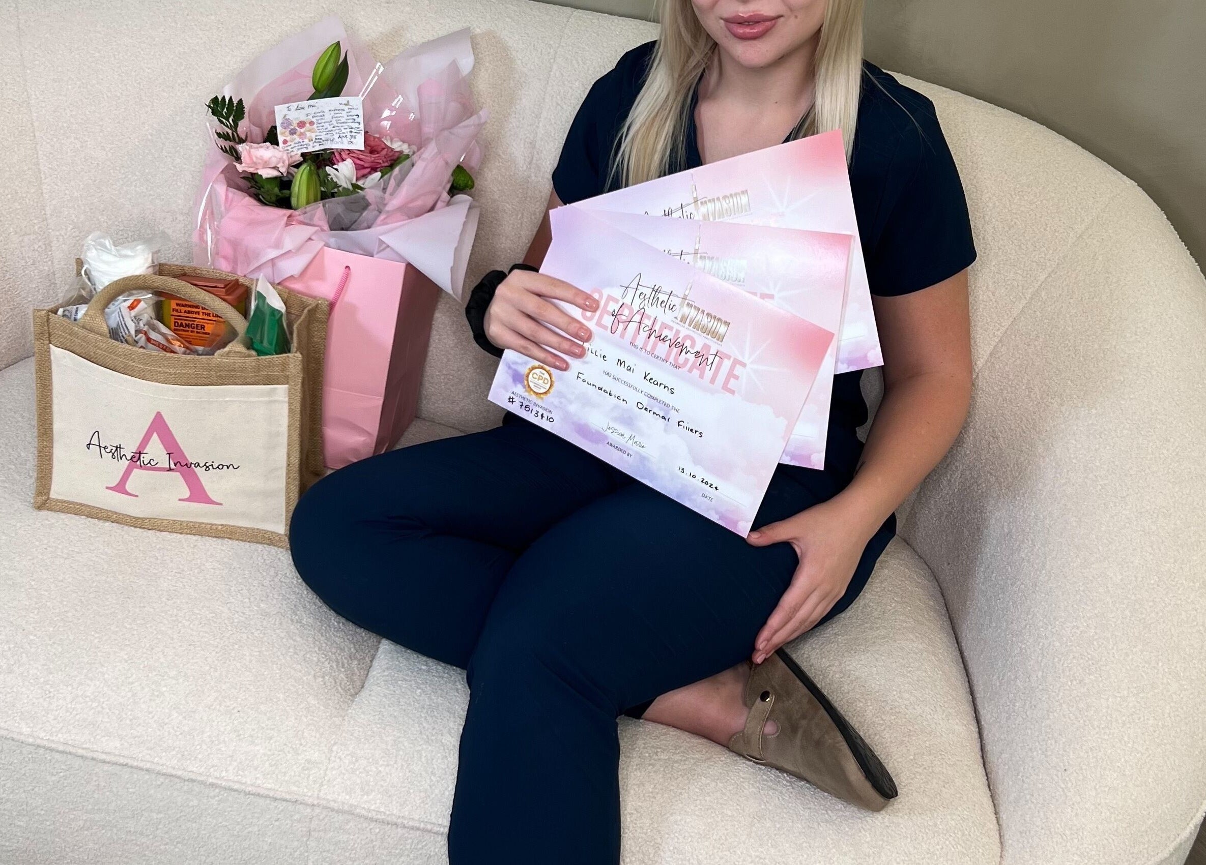 Woman holding certificates from Aesthetic Invasion, Liverpool, England, GB, seated with flowers and a branded bag.