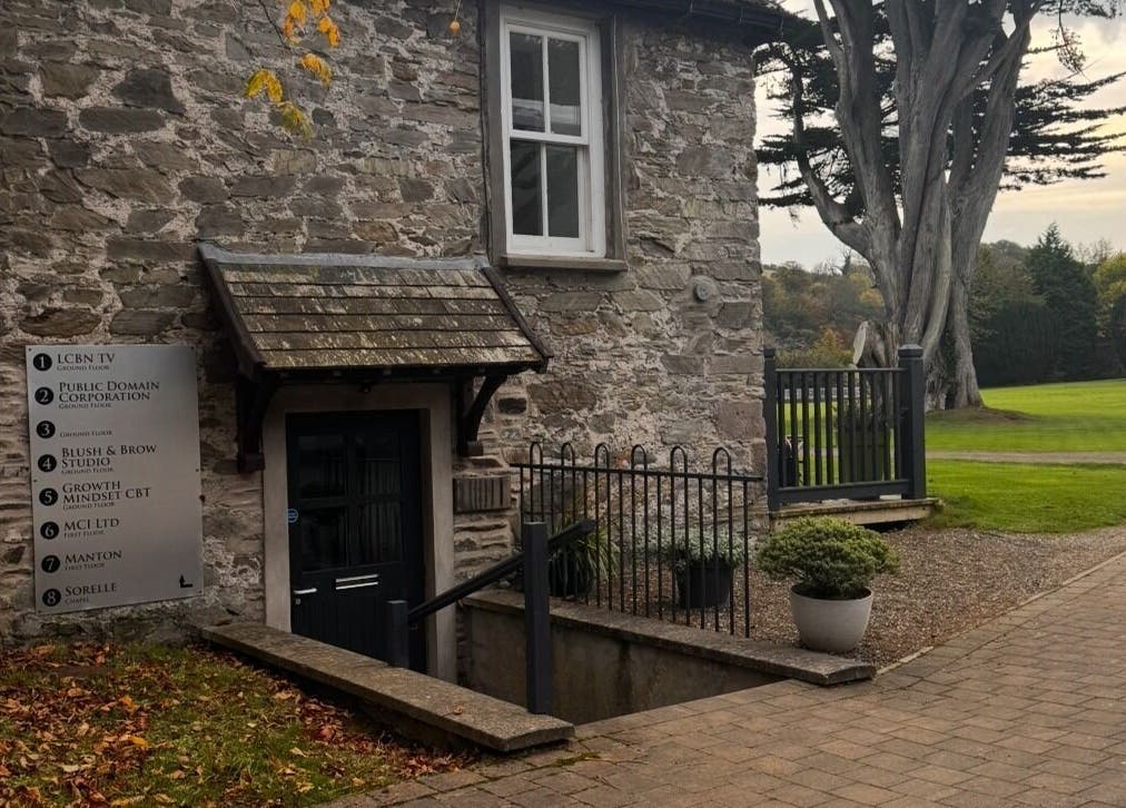 Charming stone building at MyRevibe, Douglas, IM surrounded by lush greenery and serene pathways.